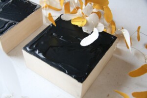 Detail of small acrylic painting on panel with yellow and white pedal like shapes on wire above.