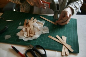 I am hammering a nail into a thin wood piece, similar to a popsicle stick, to make a hole for the wire to go through.