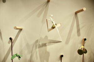 A sculpture with one long strip hung from the centre tied with mixed-media materials that are hung from a dowel.