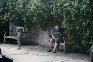 A participant is sitting on a bench by a pond recording sounds near him.