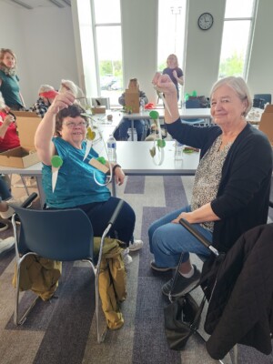 Two participants are holding their mobile sculptures while smiling at the camera