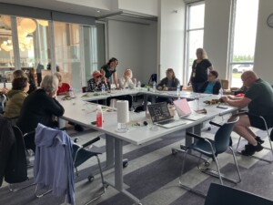 A view of the room with all the participants gathered around the table. Dawn is recording a participant's interpretation of what they are touching.