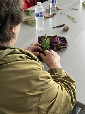 Looking over the shoulder of a participant, they are feeling the texture of a potted plant with long vertical stems.