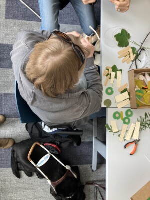 Downwards view of a participant feeling the texture of a sculpture mobile. The materials for their sculpture are laid out in front of them.