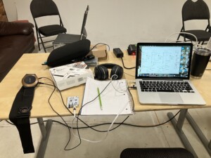 A laptop, notebook, pencil, headphones and cables on a table.