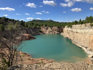 A small turquoise lake is pooling at the bottom of an abandoned quarry.