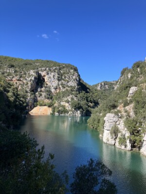 View of a gorge with turquoise water runs through shrub covered mountains.